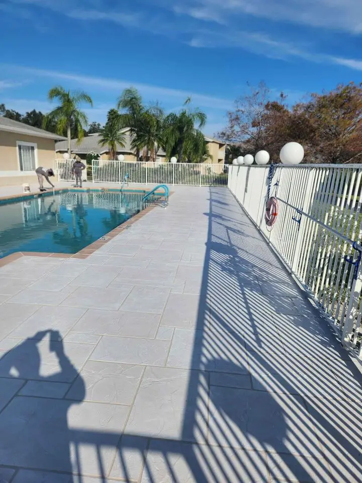 A person is kneeling on the ground, using a trowel to smooth out concrete at a busy construction site. The shadow of their outstretched arm is visible on the surface. For top-notch concrete services Miami-Dade residents trust, this scene exemplifies the expertise of Concrete Contractors Miami.